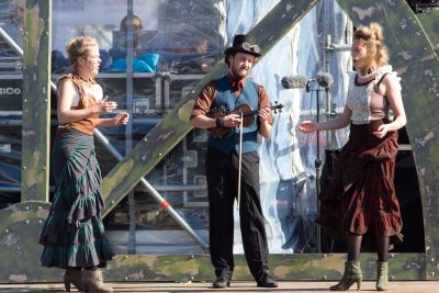 Eén man en twee vrouwen in steampunk kleding staan op podium