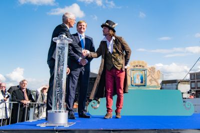 Koning Willem-Alexander, burgemeester Marco Out en man staan op podium Blauwe As