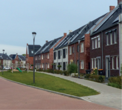 Straat met verschillende woningen in verschillende soorten steen. Op de voorgrond een groenstrook met gras en een lantaarnpaal.