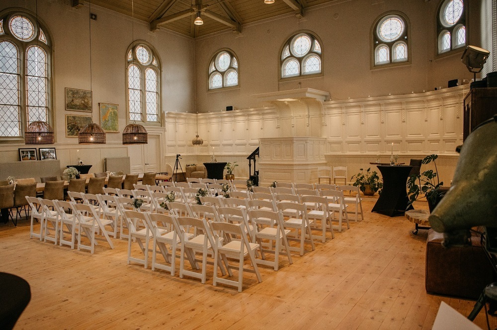 Interieur Hervormde Kapel. Witte muren, houten vloer, fraaie boogramen. De witte stoelen voor de bruiloftsgasten staan klaar.