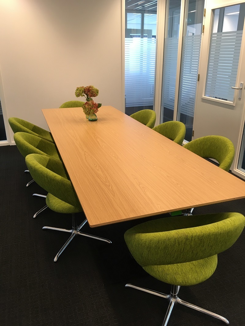 vergaderkamer met rechthoekige tafel en 8 groene stoelen rondom